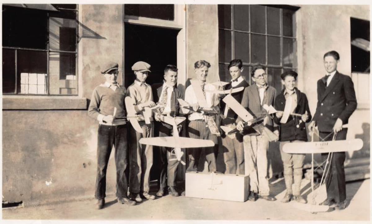 1930s photograph of boys and men lined up outside a building holding handmade model airplanes.