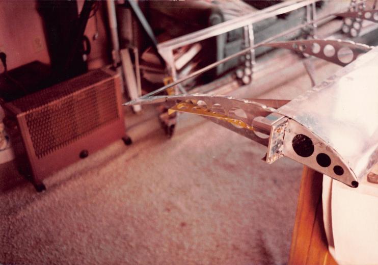 Close-up of a riveted aluminum rotor rib drilled with lightening holes, resting on living-room carpet, an electric heater in the background.